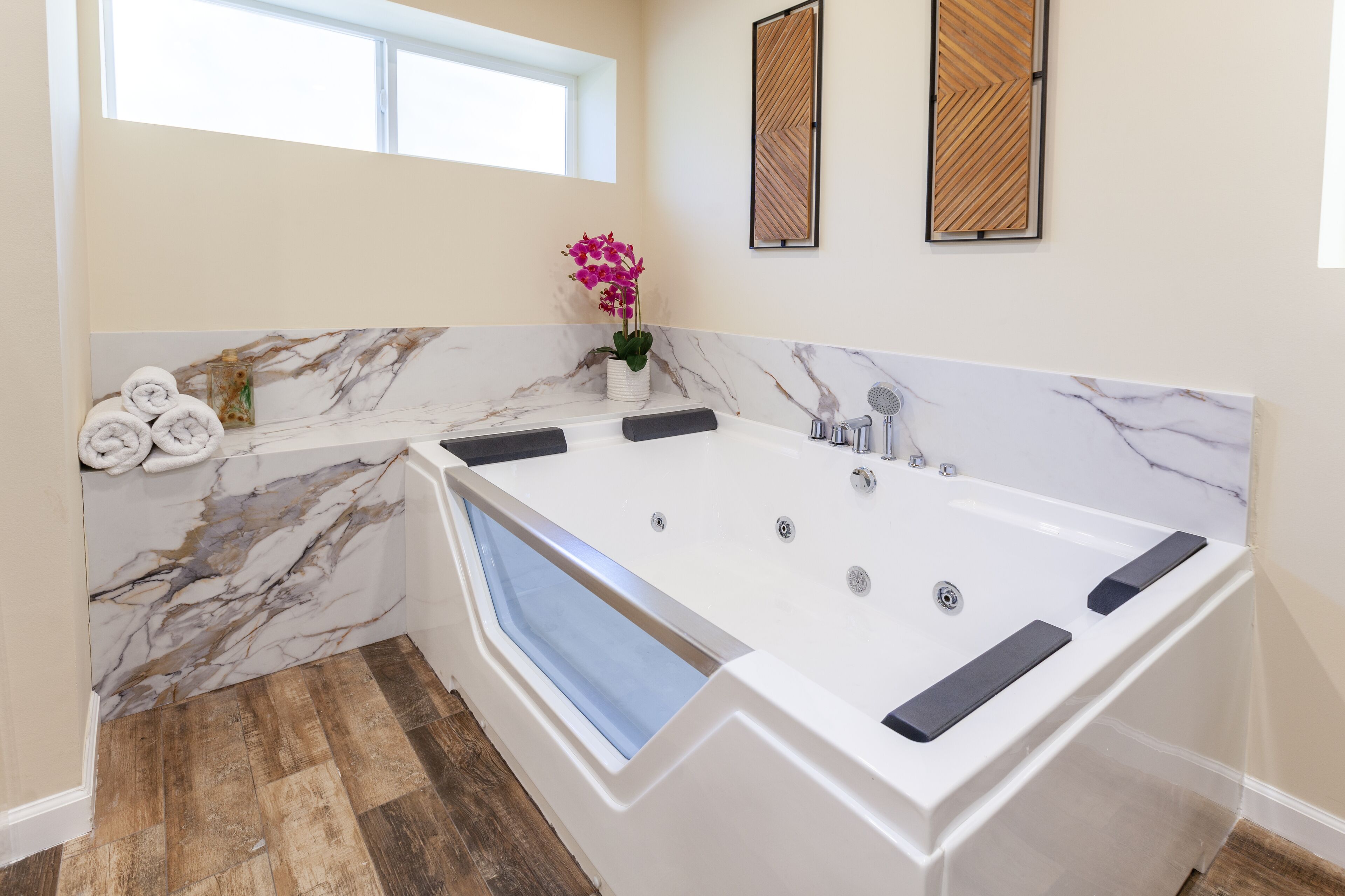 A modern bathroom with a large bathtub, marble walls, and a window.