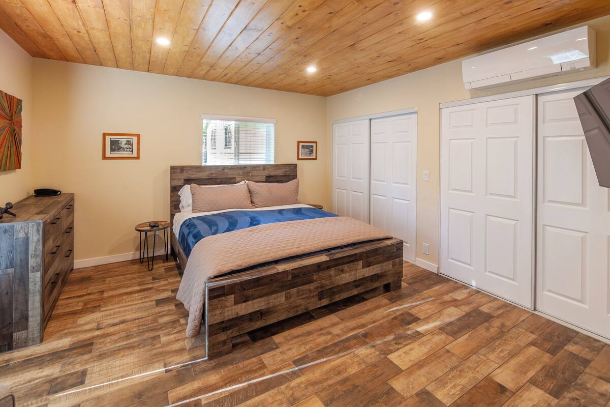 A bedroom with a wooden bed, a dresser, a window, and white closets.