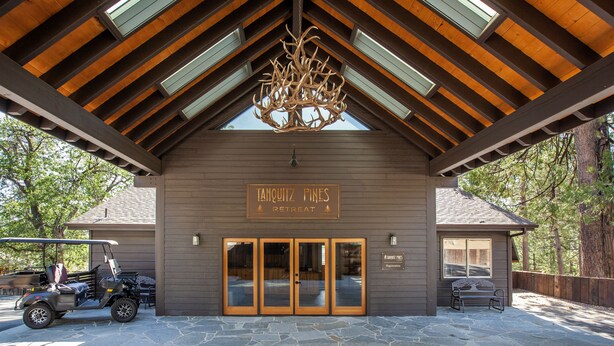 Indgangsparti til et lodge med en brostensbelagt indkørsel, en golfvogn og et skilt der siger "Taquintz Pines Retreat".
