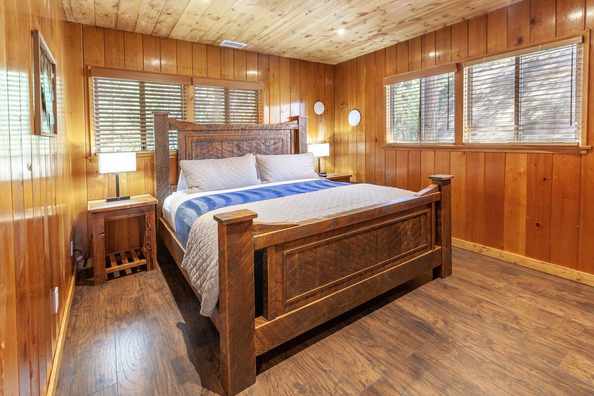 A wooden-paneled bedroom with a large bed, two bedside tables, and a window with blinds.