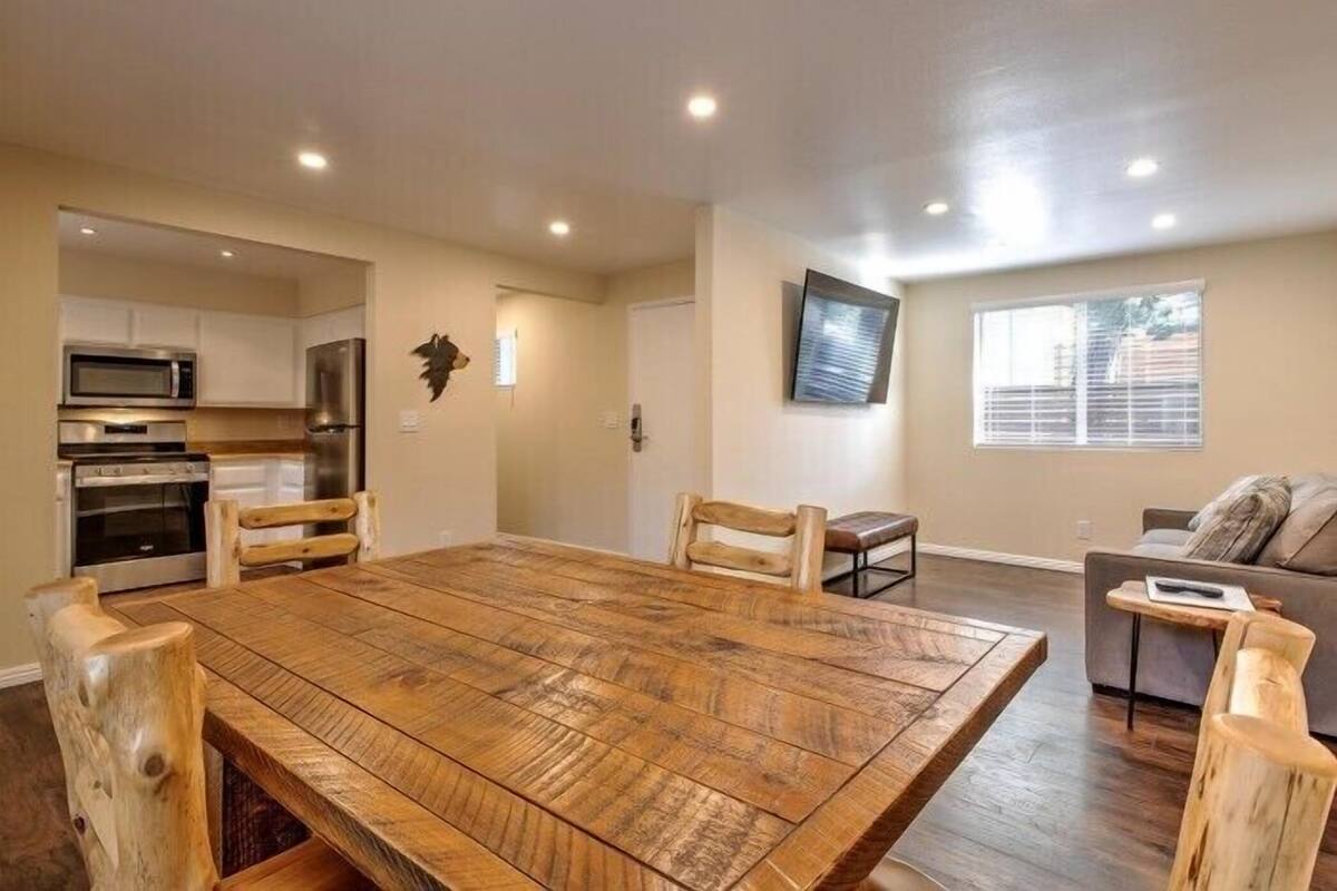 A spacious living room with a large wooden dining table, a kitchen area with modern appliances, and a comfortable seating area with a sofa and chairs.