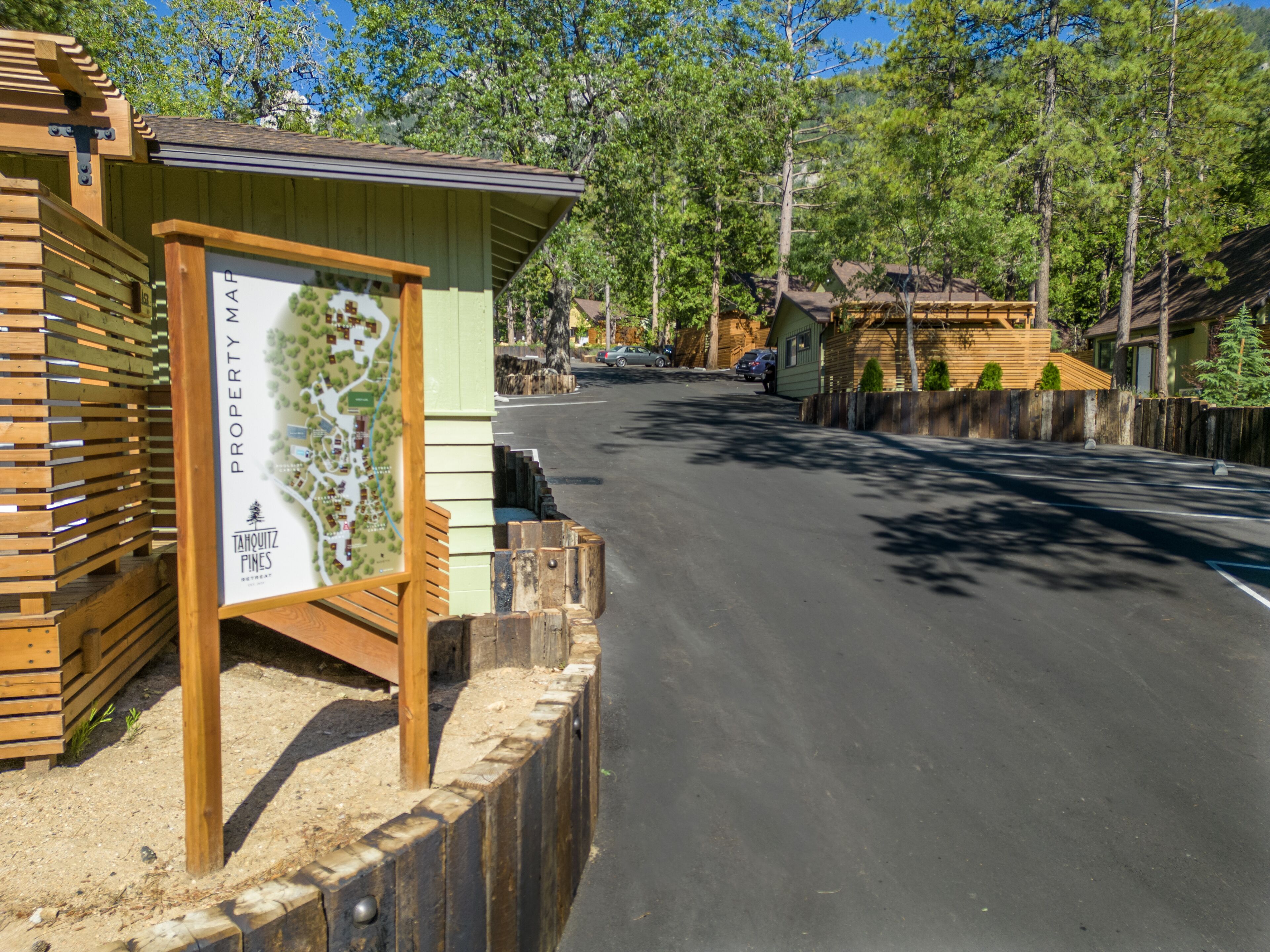 Una cabaña de madera con un cartel de mapa, rodeada de árboles y un camino pavimentado.