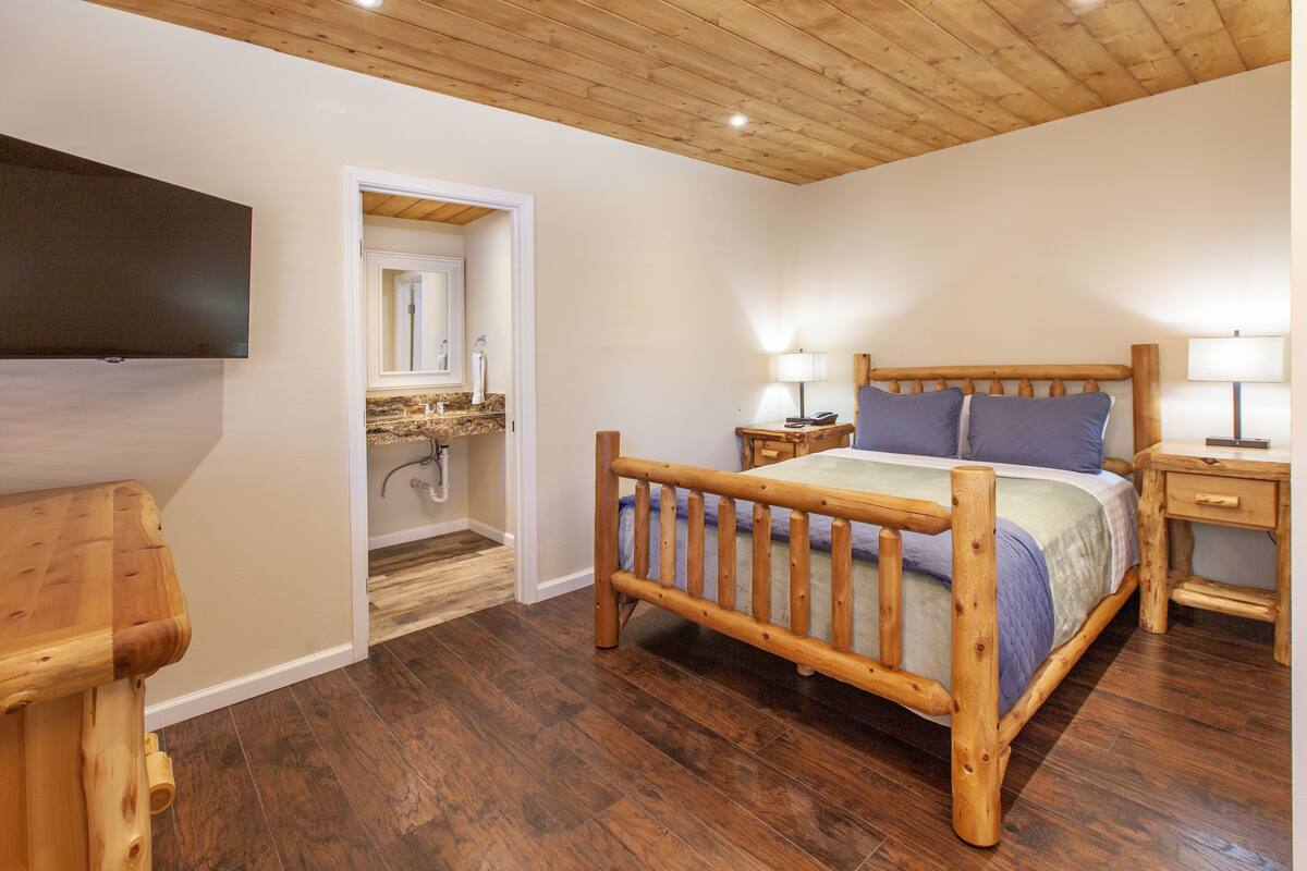 A bedroom with a wooden bed frame, a TV mounted on the wall, and a wooden floor.