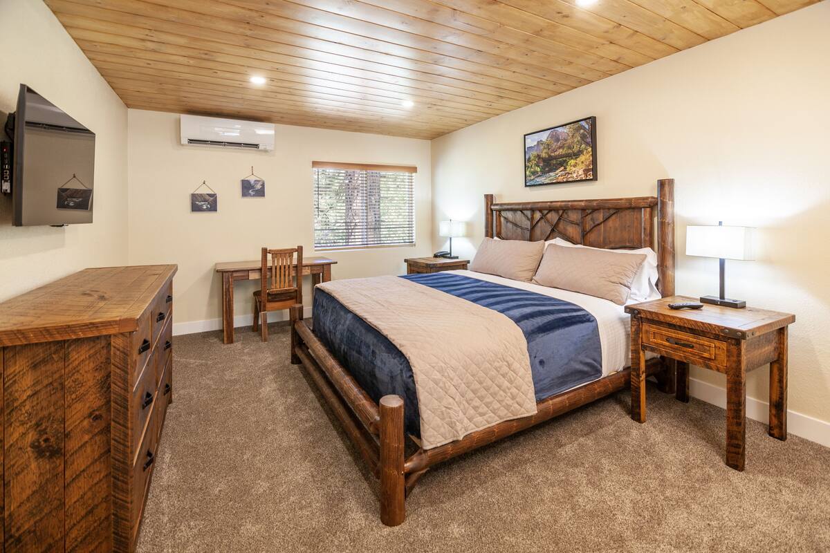 A bedroom with a wooden bed, a dresser, a nightstand, and a TV mounted on the wall.
