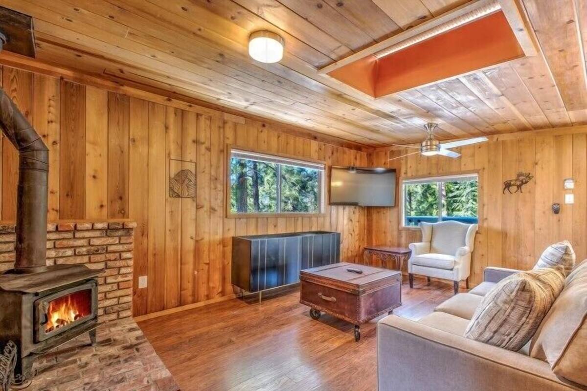 A cozy cabin interior with a stone fireplace, wooden walls, a sofa, and a television.