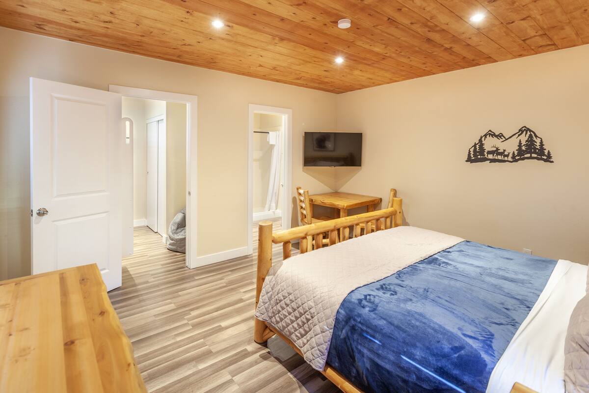 A bedroom with a wooden bed, a TV mounted on the wall, and a wooden table.