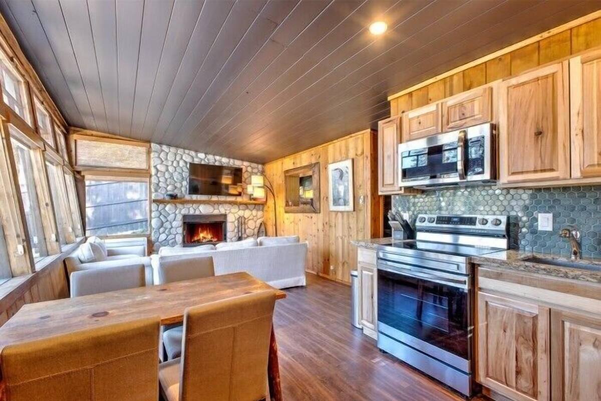 A cozy cabin interior with a stone fireplace, wooden cabinets, a dining area, and a kitchen with modern appliances.