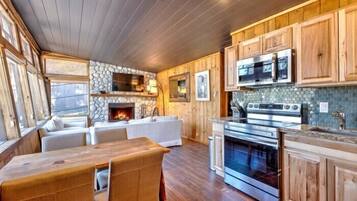 A cozy cabin interior with a stone fireplace, wooden cabinets, a dining area, and a kitchen with modern appliances.