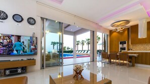 Un salón moderno con televisión, una mesa de centro de cristal y vista a la piscina.