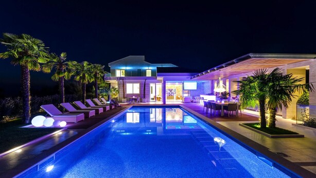 Un área moderna junto a la piscina con sillones de descanso y una piscina, rodeada de palmeras y un edificio bien iluminado.