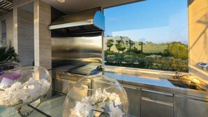 Una cocina moderna con extractor de acero inoxidable, un ventanal con vista a la vegetación y dos invernaderos con flores.