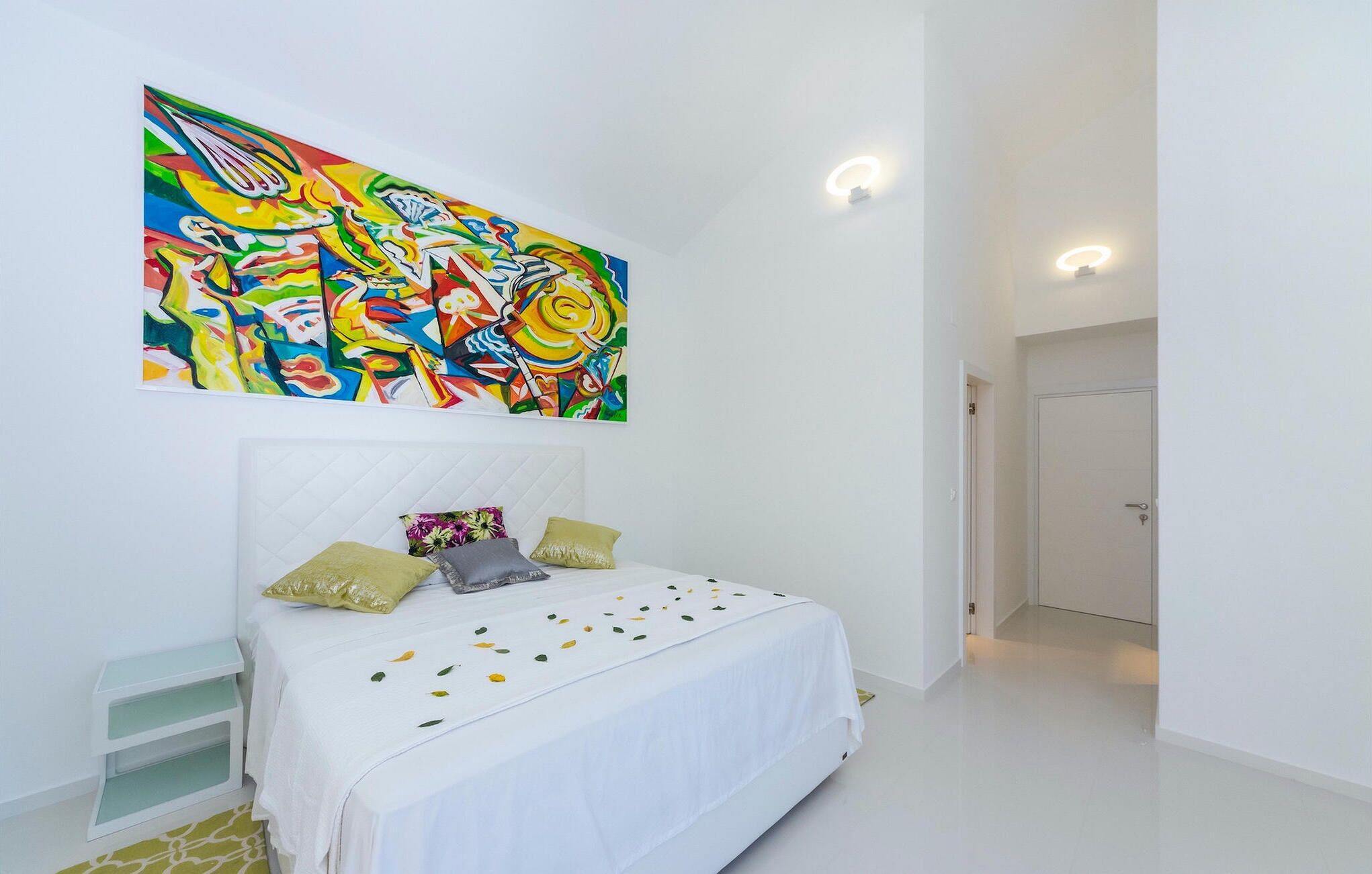 Quarto com cama branca, pintura abstrata colorida e porta branca.
