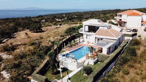 Una casa moderna de dos pisos con piscina, rodeada de exuberante vegetación y vista al mar.