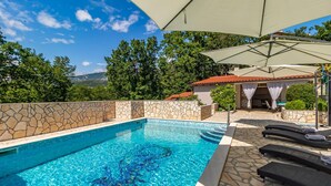 Una piscina con paredes de piedra, sillas de descanso y una zona de estar cubierta con vistas al paisaje.