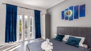 Habitación de hotel moderna con una cama grande, cabecera gris y vistas al exterior a través de una puerta corrediza de vidrio.