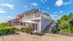 Una casa de dos pisos con un balcón, una escalera y un jardín.