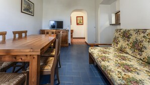 A dining area with a wooden table and chairs, a sofa with a floral pattern, a television, and framed artwork on the walls. - Orbetello Giannella Apartment (Orbetello)