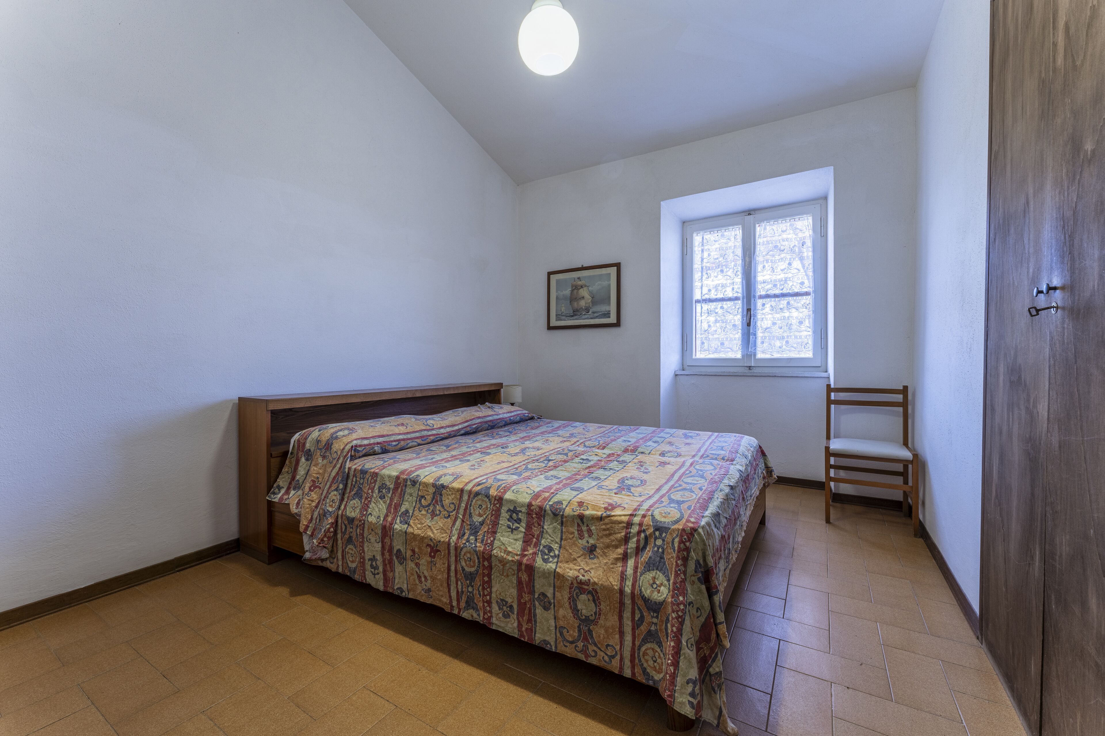 Ein Schlafzimmer mit Bett, Fenster, Sessel und Kleiderschrank.