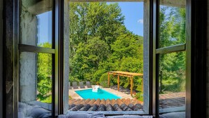 Une vue depuis une fenêtre donnant sur une pièce avec une piscine, un espace salon extérieur et une pergola.