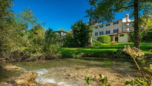 Un ruisseau limpide serpente à travers un jardin luxuriant, avec un bâtiment en pierre en arrière-plan.
