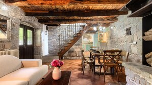 Un intérieur rustique avec des murs en pierre, un escalier en bois, un coin repas et un canapé.