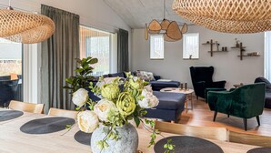 Ein modernes Wohnzimmer mit Essbereich, ausgestattet mit einer Steinvase mit Blumen, gewobenen Leuchten und einem dunkelblauen Sofa.