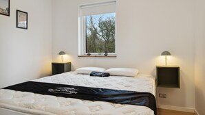 Ein Schlafzimmer mit einem Bett, zwei Nachttischen, einem Fenster mit Blick auf Bäume und gerahmten Bildern an der Wand.