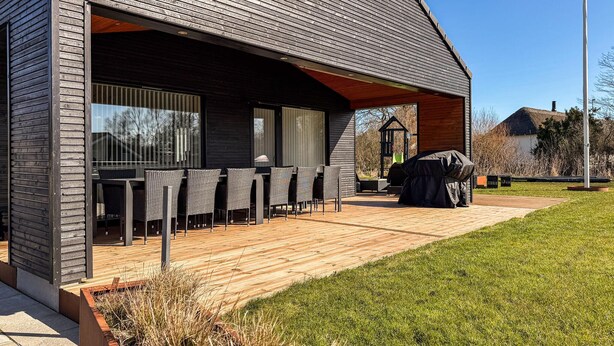Ein modernes Gebäude mit einer überdachten Außenlounge, einem Grill und einer Holzterrasse.
