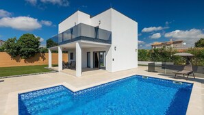 Ett modernt hus i två våningar med en swimmingpool, en uteplats och en klarblå himmel.