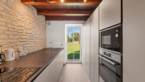 A modern kitchen with a stone wall, wooden ceiling beams, a Bosch microwave, and a view to the outdoors.
