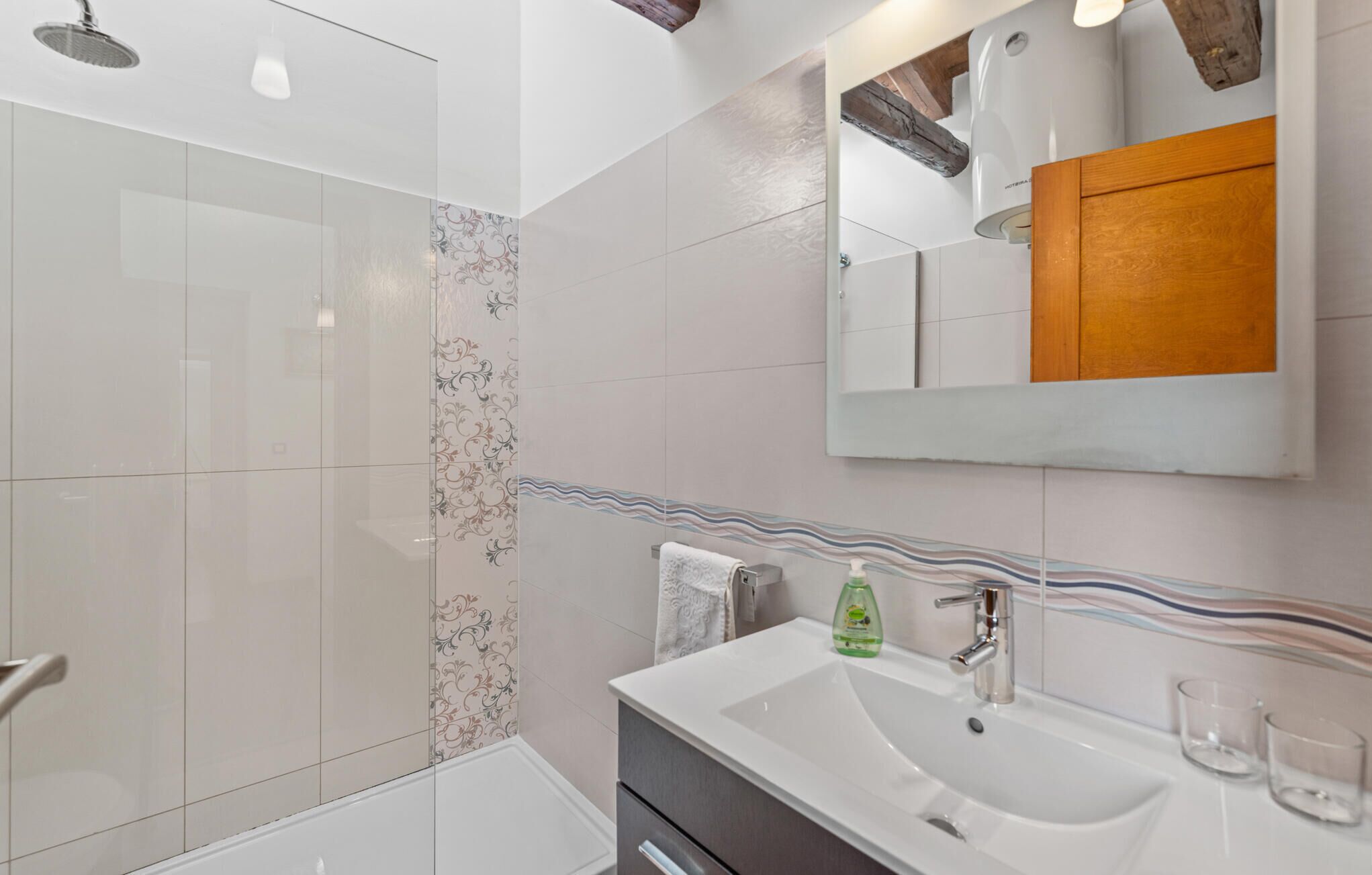 Een moderne badkamer met een glazen douche, een witte wastafel met spiegel erboven en een houten kastje.