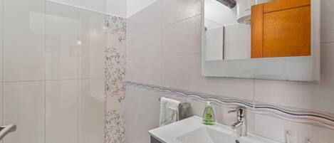 Een moderne badkamer met een glazen douche, een witte wastafel met spiegel erboven en een houten kastje.