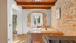 A dining area with a stone wall, wooden ceiling, and a view of a garden through a door.