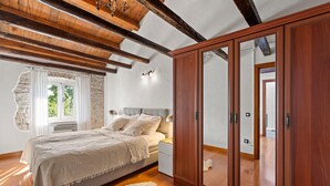 A bedroom with a large wooden wardrobe, a bed with a white bedspread, and a stone wall.