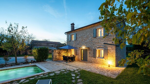 A stone house with a swimming pool, outdoor seating, and a well-maintained garden.