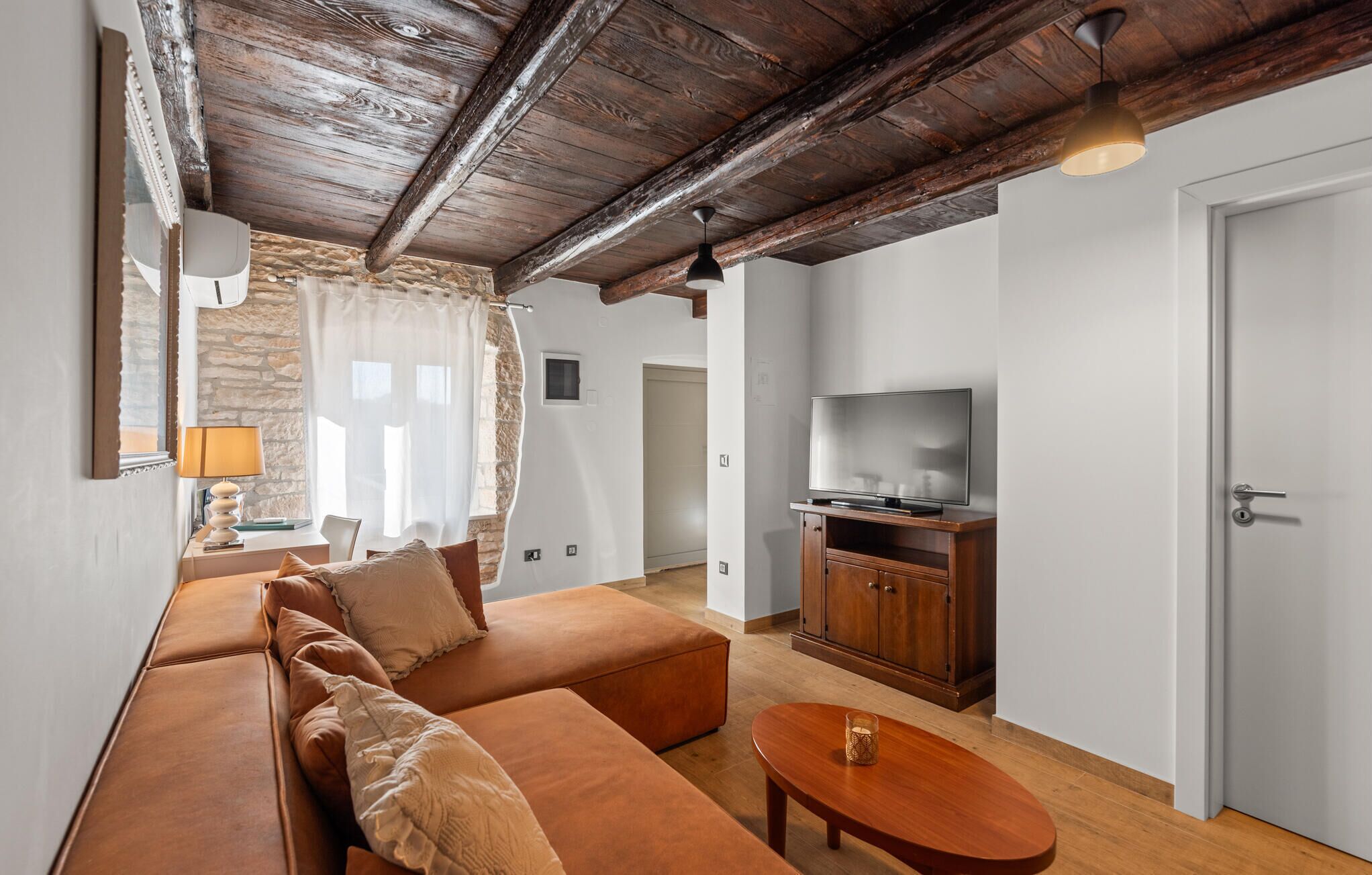 A living room with a wooden ceiling, a sofa set, a television on a wooden cabinet, and a small table.