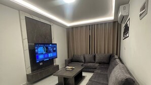 A modern living room with a sectional sofa, a flat-screen TV, a coffee table, and a marble-tiled floor.