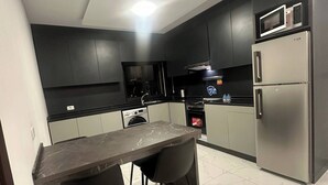 A modern kitchen with dark cabinets, a marble countertop, and a built-in microwave.