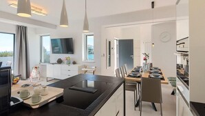 A modern kitchen with a central island, dining area, and a TV mounted on the wall. - Gorgeous home in Pula (Pula)