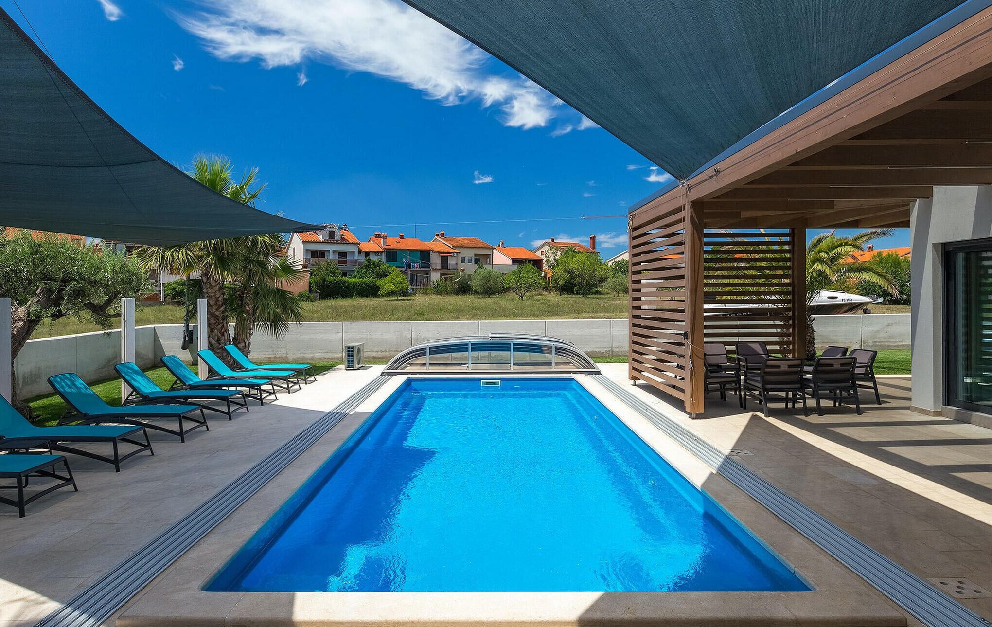 En swimmingpool med blåt vand, omgivet af liggestole og et skyggefuldt område.