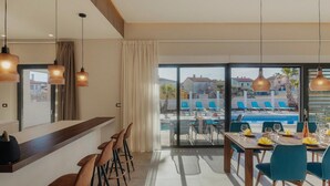 Un espace repas moderne avec vue sur la piscine, comprenant un bar, des sièges et de grandes fenêtres.