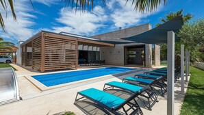 Un espace piscine extérieur moderne, doté de chaises longues et d’un patio couvert.