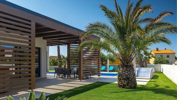Une terrasse extérieure moderne, dotée d’une piscine, de palmiers et d’un espace salon abrité.