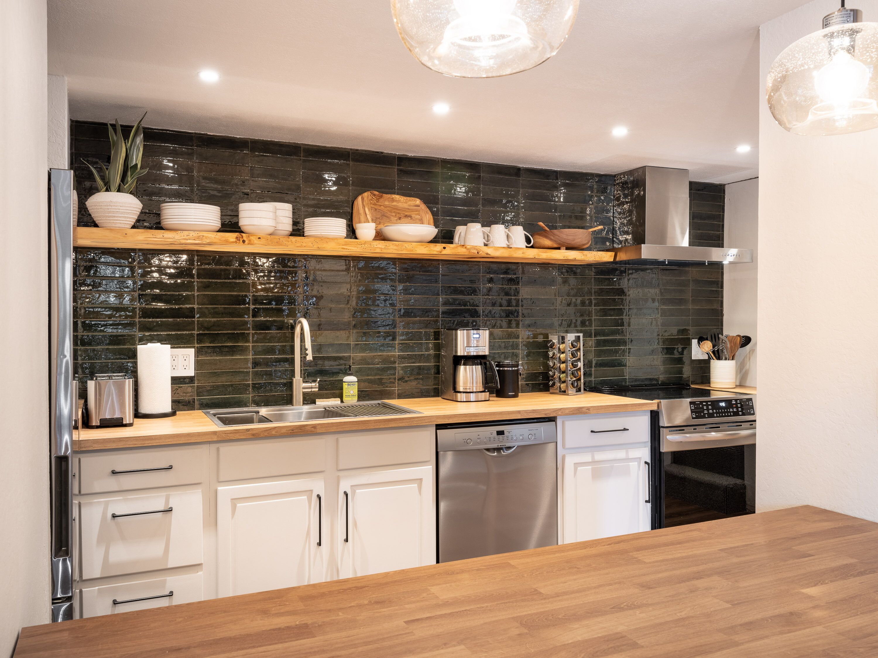 A modern kitchen with a wooden countertop, stainless steel appliances, and a black tiled backsplash.