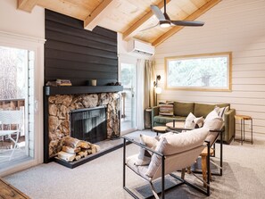 A cozy living room with a stone fireplace, a ceiling fan, and a large window.