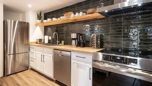 Een moderne keuken met roestvrijstalen apparatuur, een houten aanrecht en een zwart betegelde spatwand.