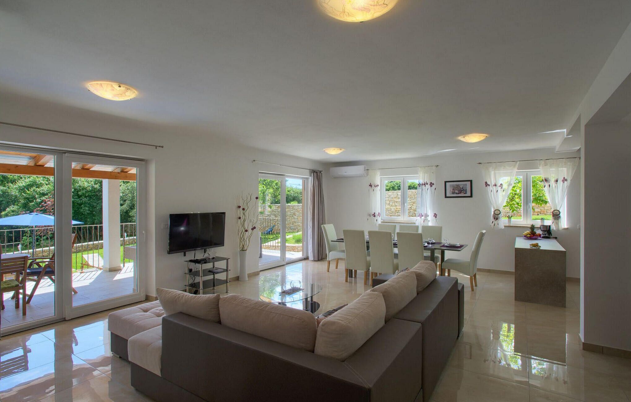 A spacious living room with a large sofa, a flat-screen TV, and a dining area with a table and chairs.