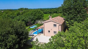 Une maison à deux étages avec une piscine, entourée d’une végétation luxuriante.
