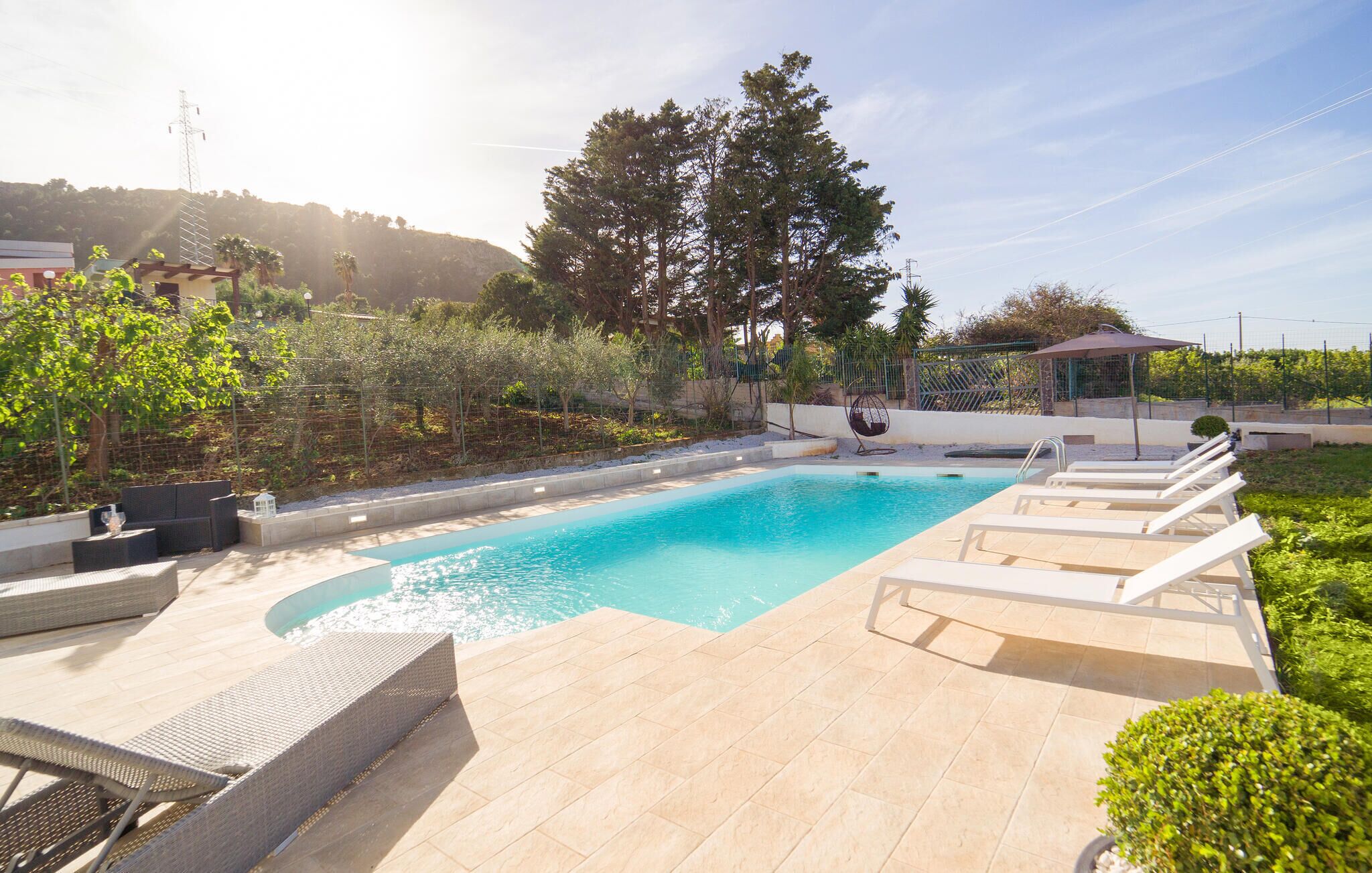 Una piscina rectangular con solárium empedrado, rodeada de sillones de descanso y una pérgola.