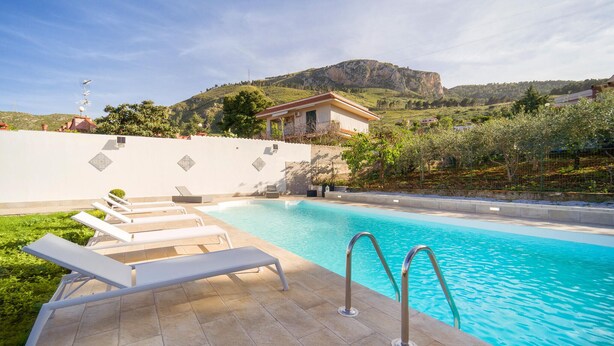 A swimming pool with lounge chairs, a clear view of a mountain, and a building in the background. - Amazing home in Altavilla Milicia (Altavilla Milicia)